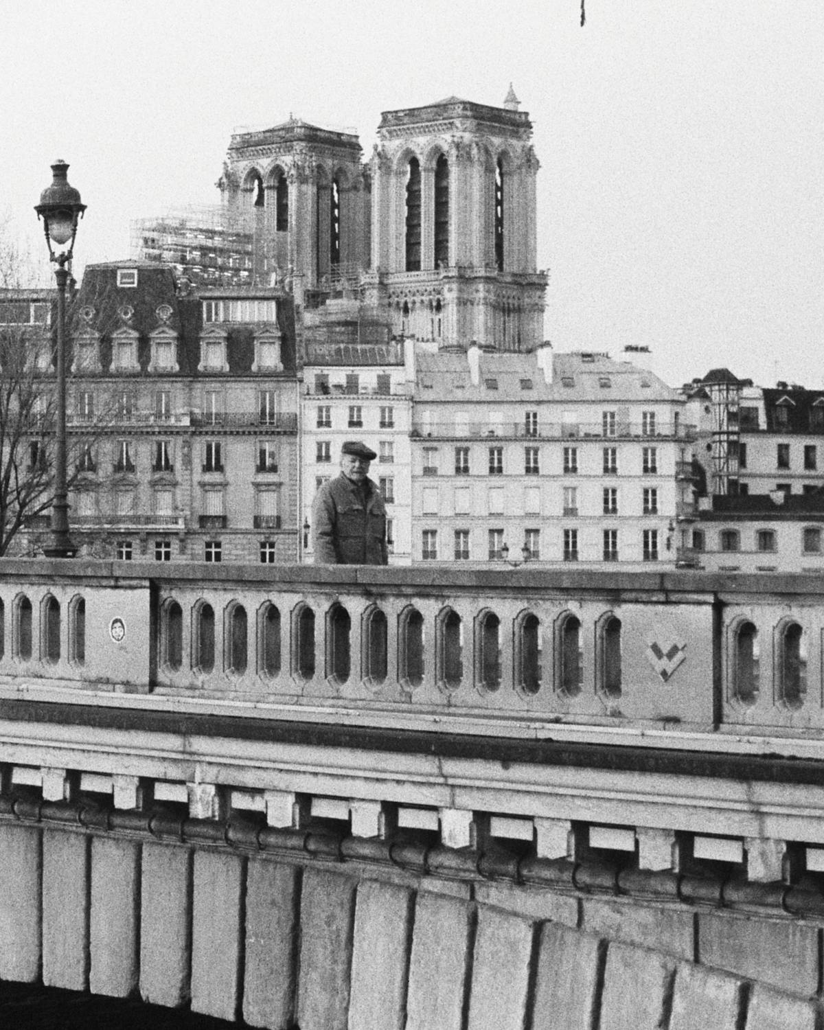 An old man crossing a bridge in front of Notre Dame