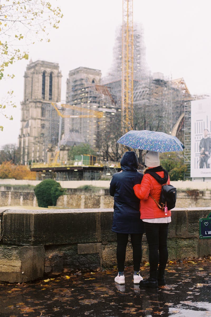 A couple under an umbrella looking at the back of Notre Dame, covered in scaffolding