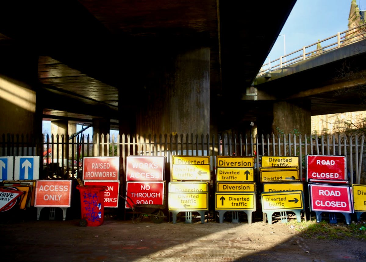 A collection of construction signs under an overpass.